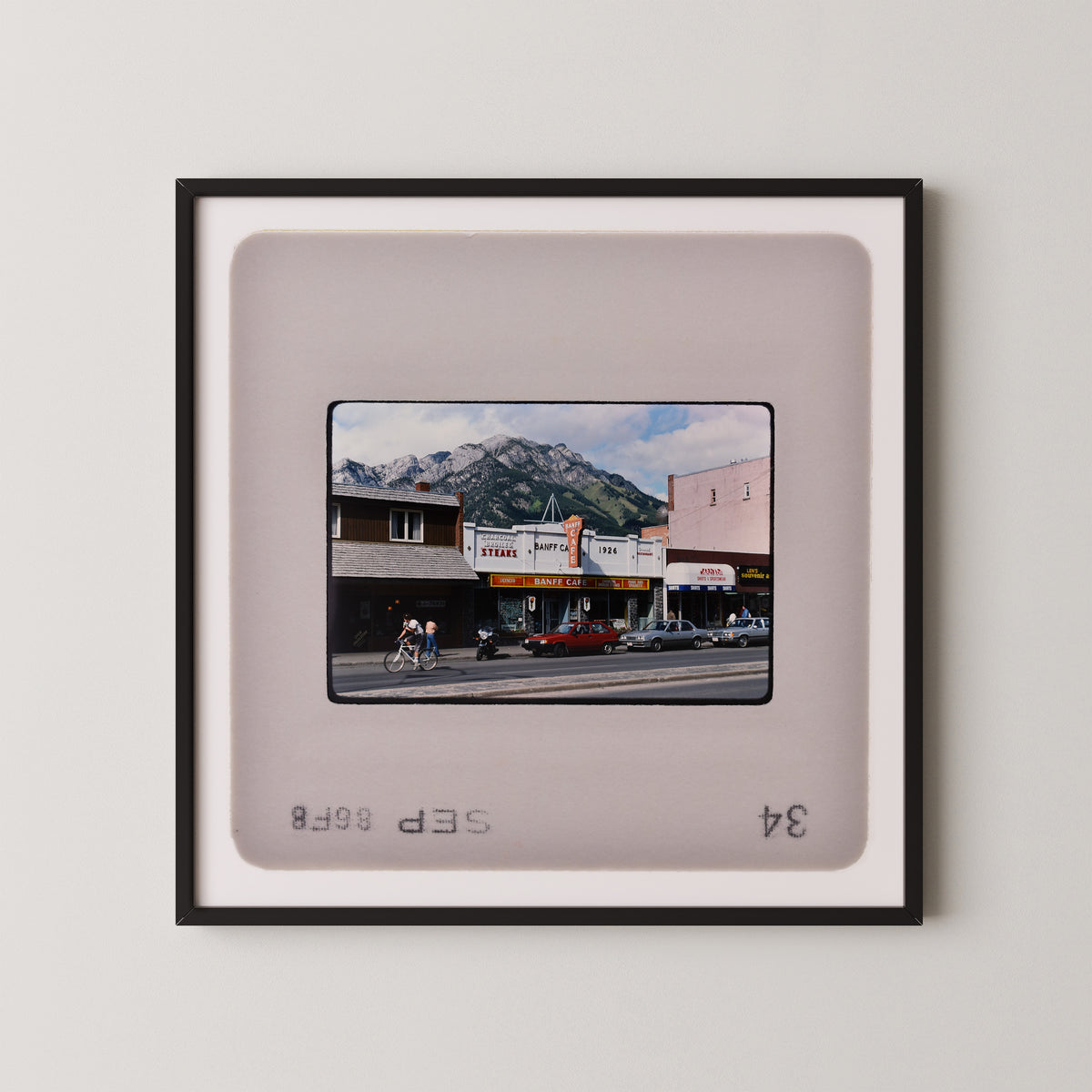 The image is a framed photograph of a city street scene with buildings, cars, and people.