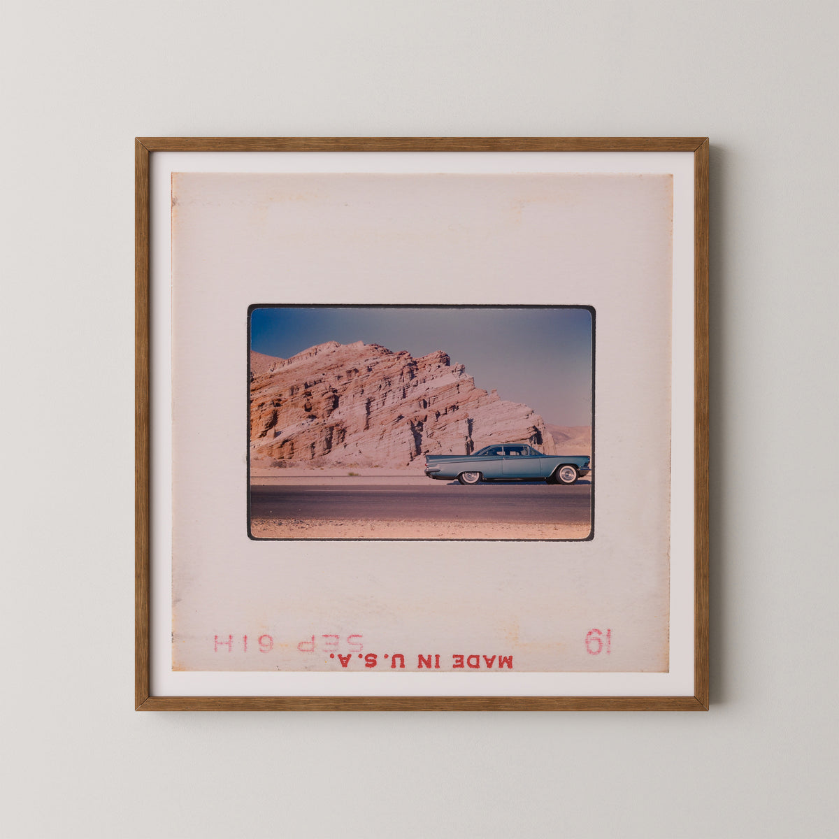 A framed photograph of a vintage car driving on a road, with a rocky mountain landscape in the background.