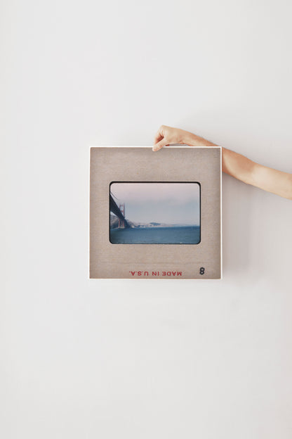 A person's hand is holding a framed photograph of a bridge in the background.