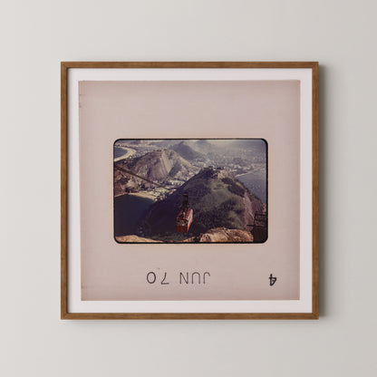 The image is a framed photograph of a mountainous landscape with a red building on a cliff.