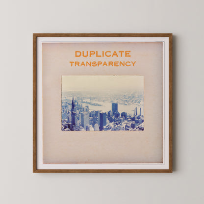 The image is a framed print of a cityscape, with the text "DUPLICATE TRANSPARENCY" prominently displayed above the photograph.