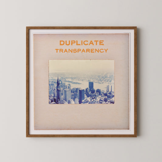 The image is a framed print of a cityscape, with the text "DUPLICATE TRANSPARENCY" prominently displayed above the photograph.