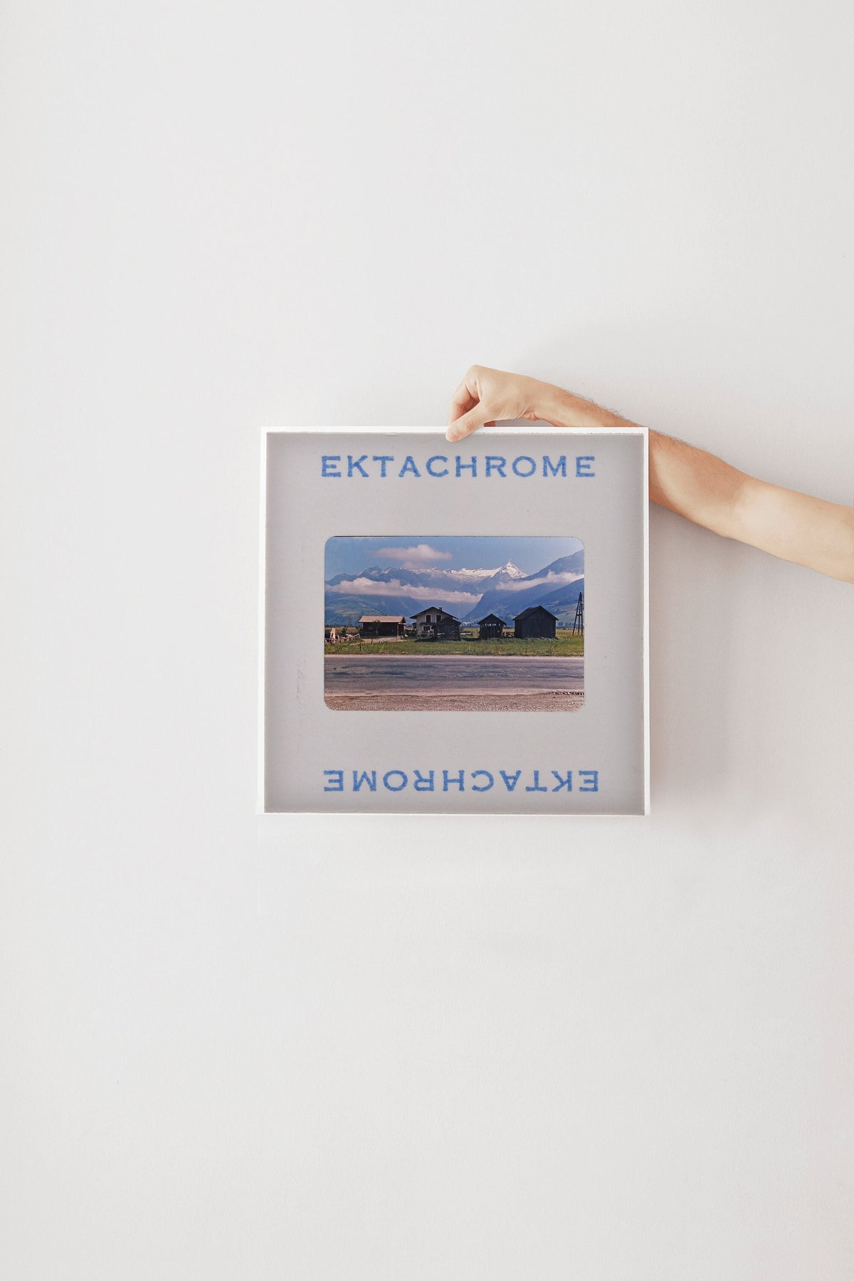 A person's hand is holding a framed photograph of a rural landscape, with the text "Ektachrome" and "Ektachrome" visible on the frame.