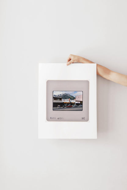 A person's hand is holding a framed photograph of a building with a mountain in the background.