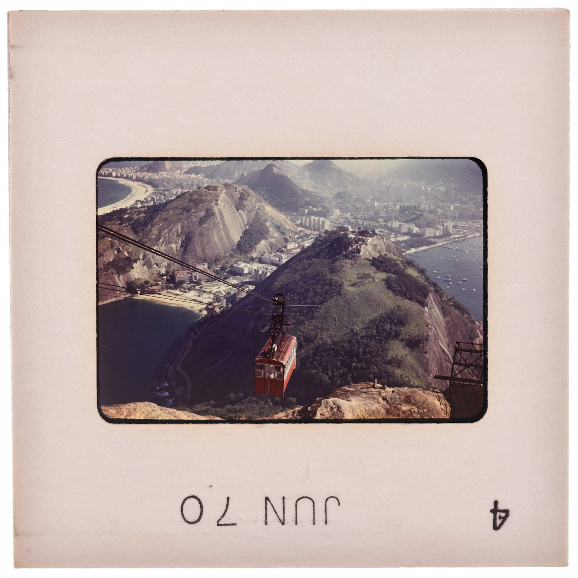 A red cable car is suspended above a mountainous landscape, with a city visible in the background.