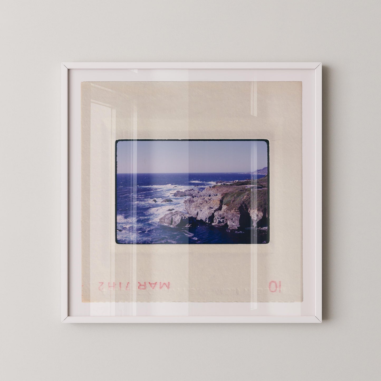 Vintage 1971 Kodachrome slide photograph of the Carmel California coastline, showing dramatic rocky cliffs and outcroppings meeting deep cobalt Pacific Ocean waters, with white surf, a green headland, and a small structure visible at the cliff's edge. Printed as a giclée fine art print on archival matte paper.