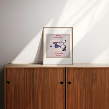 a framed artwork with a blue and white abstract design, placed on a wooden cabinet or shelf against a white wall.