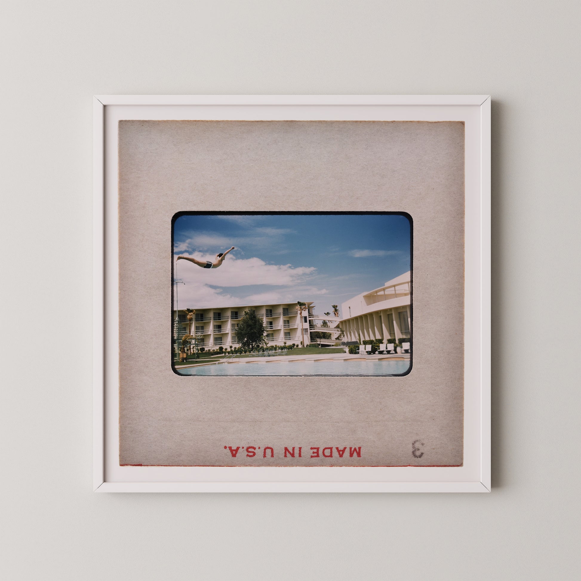 A framed photograph of a person diving off a diving board at a pool, with a hotel building visible in the background.