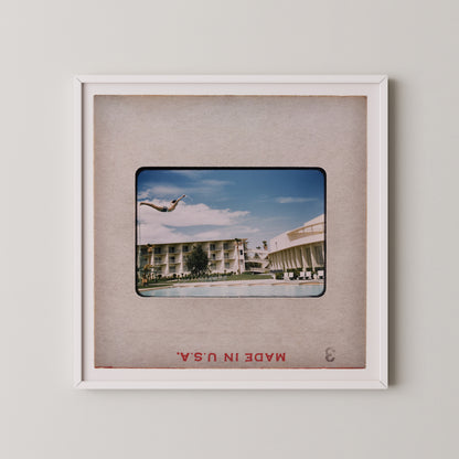 A framed photograph of a person diving off a diving board at a pool, with a hotel building visible in the background.