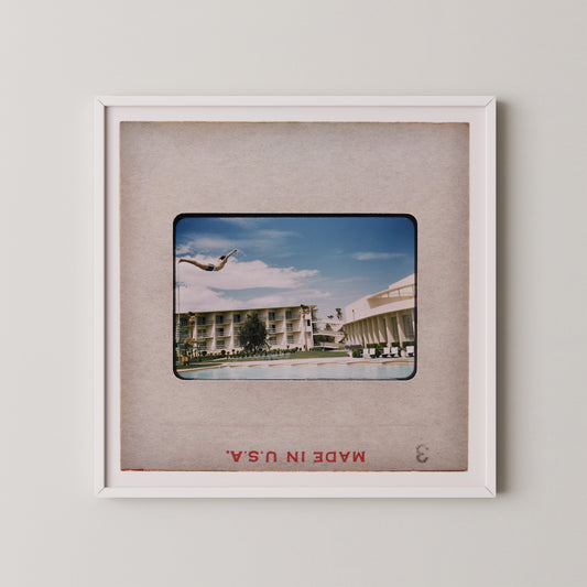 A framed photograph of a person diving off a diving board at a pool, with a hotel building visible in the background.