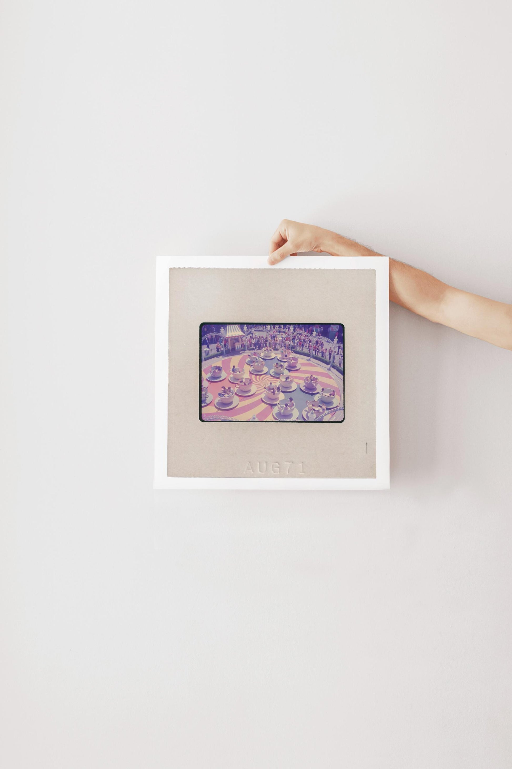 A person's hand is holding a framed picture of a colorful, abstract image on a white wall.