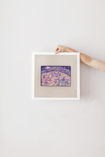 A person's hand is holding a framed picture of a colorful, abstract image on a white wall.