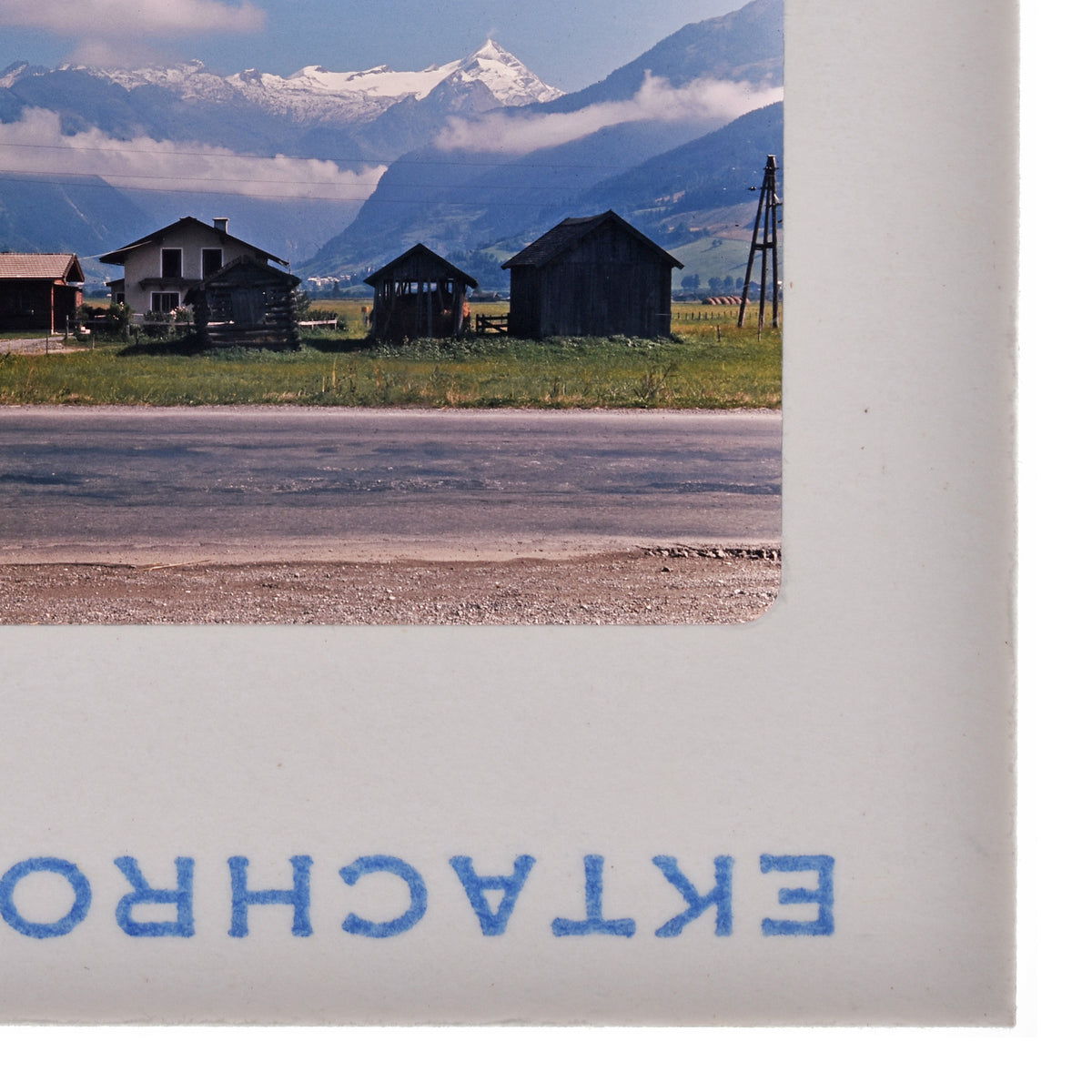 a rural landscape with a road, buildings, and mountains in the background.
