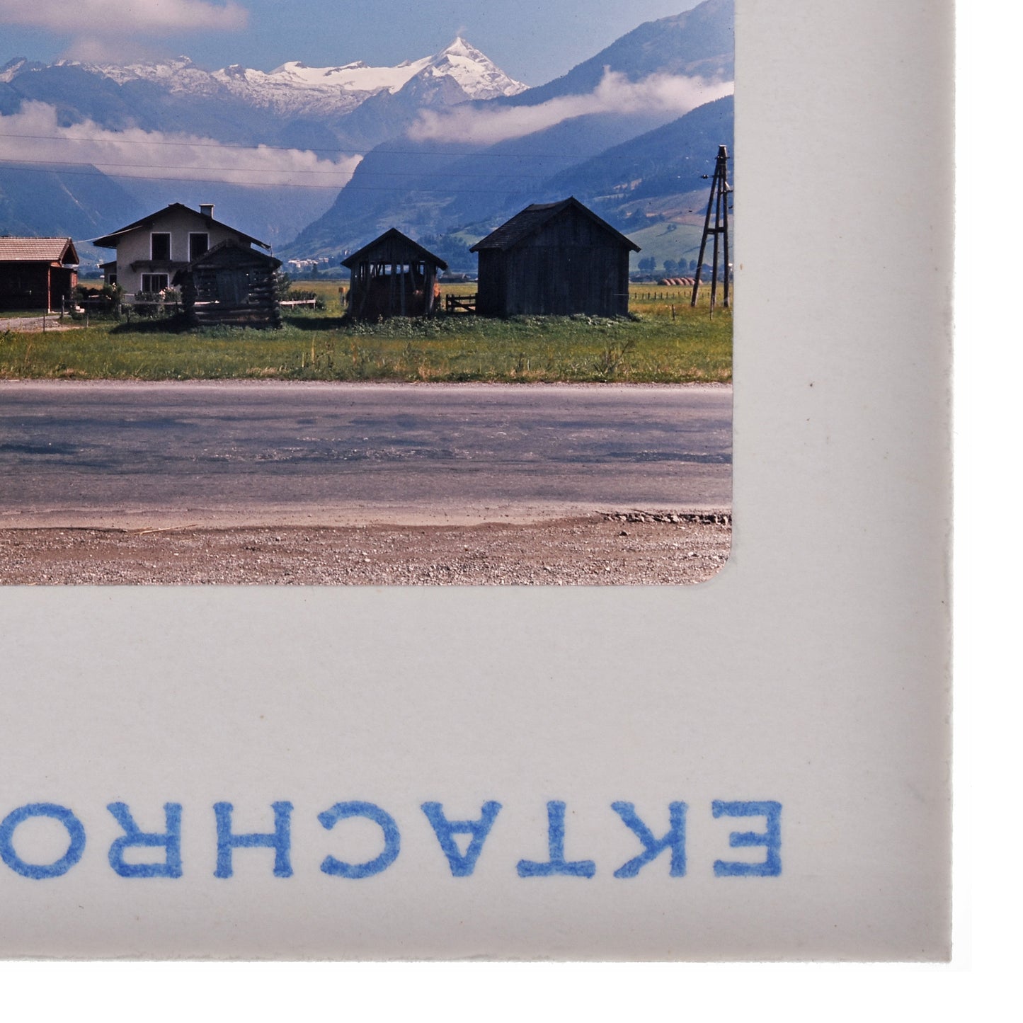 a rural landscape with a road, buildings, and mountains in the background.