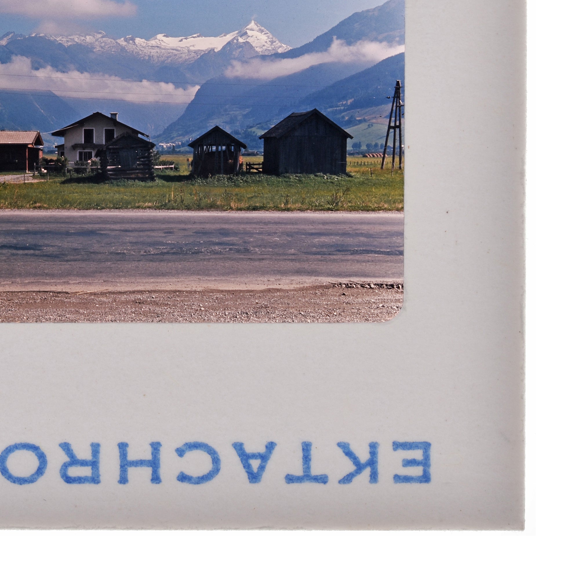 a rural landscape with a road, buildings, and mountains in the background.
